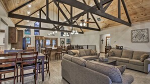 A spacious living area with a high ceiling, wooden beams, a sectional sofa, and a dining table with chairs. - Lake View | Game Room | King Beds | Hot Tub | Pool (Branson)