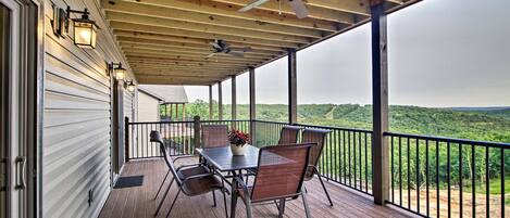 A covered outdoor deck with a table and chairs, a ceiling fan, and a view of the landscape.