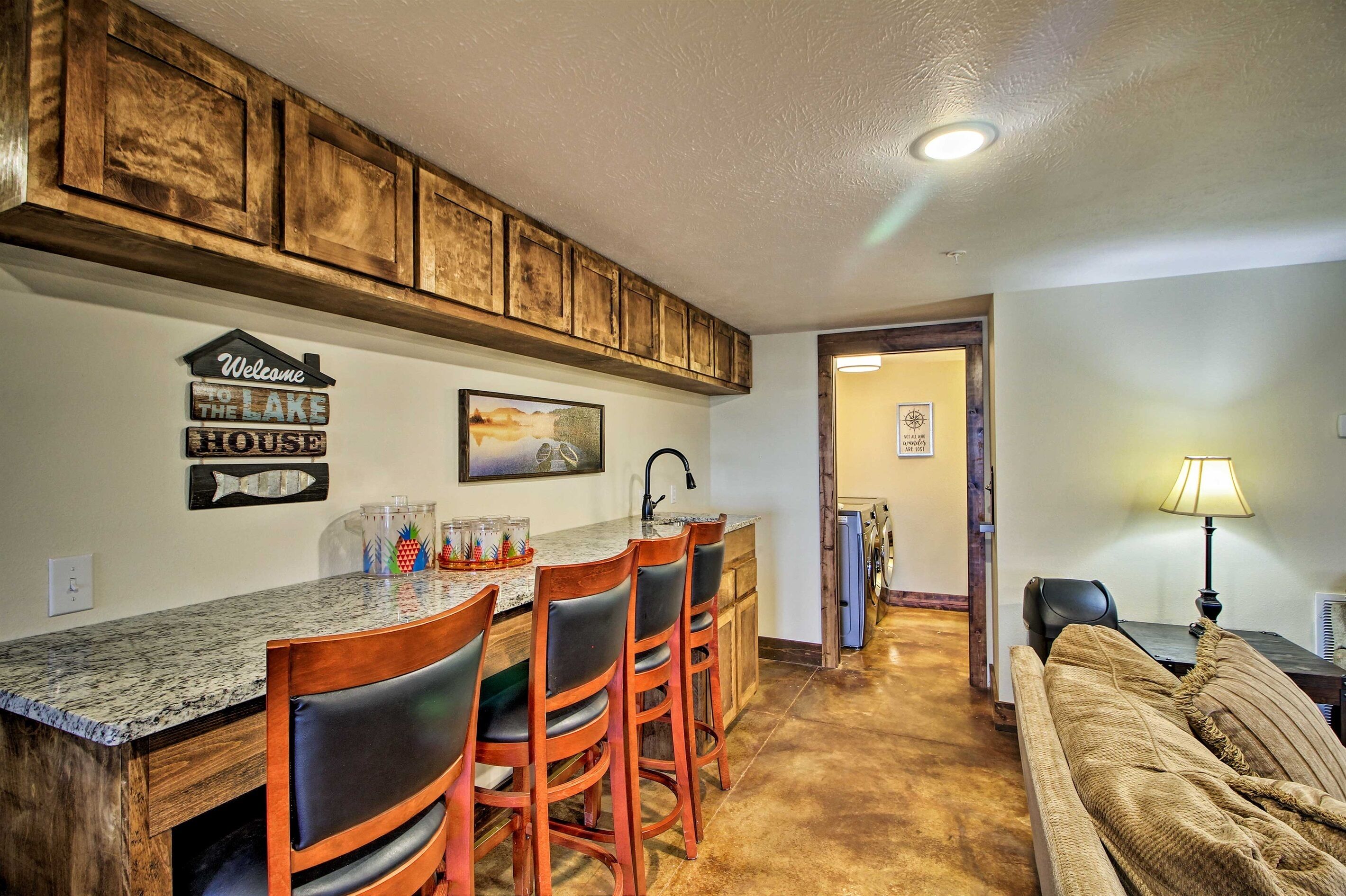 Une cuisine avec un coin bar, des meubles en bois, un panneau d’accueil et un tableau.