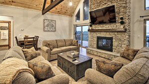 A spacious living room with a stone fireplace, a large flat-screen TV mounted on the wall, and a cozy seating area with multiple couches and a coffee table. - Lake View | Game Room | King Beds | Hot Tub | Pool (Branson)