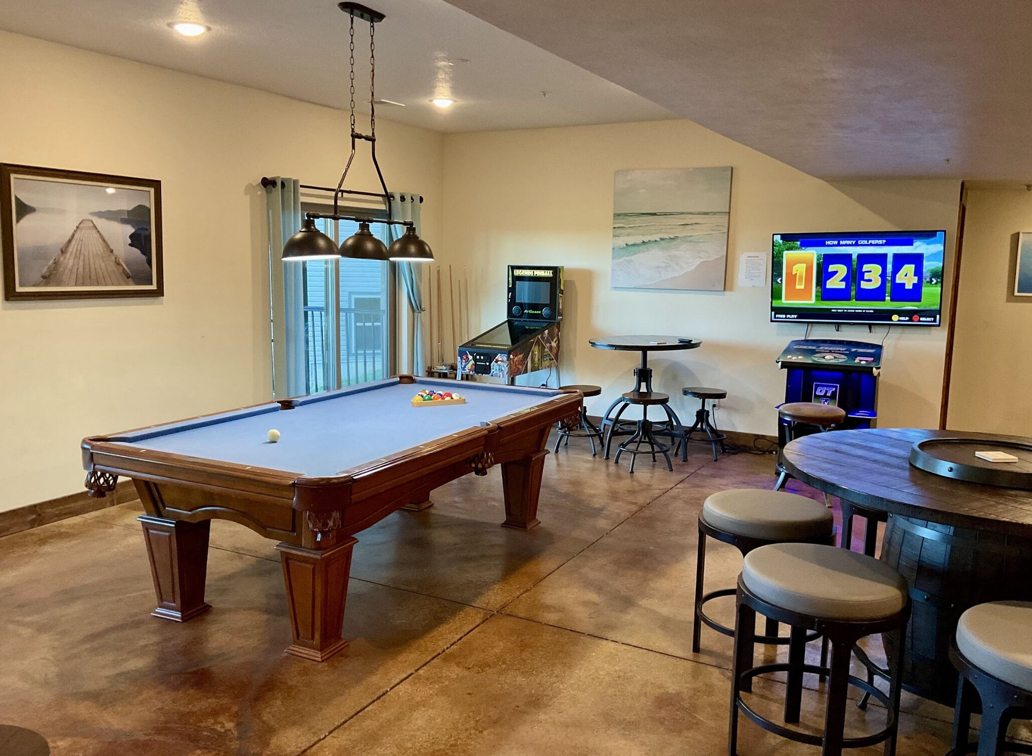 A pool table with a billiards cue rack, a bar area with stools, and a television displaying a sports game.
