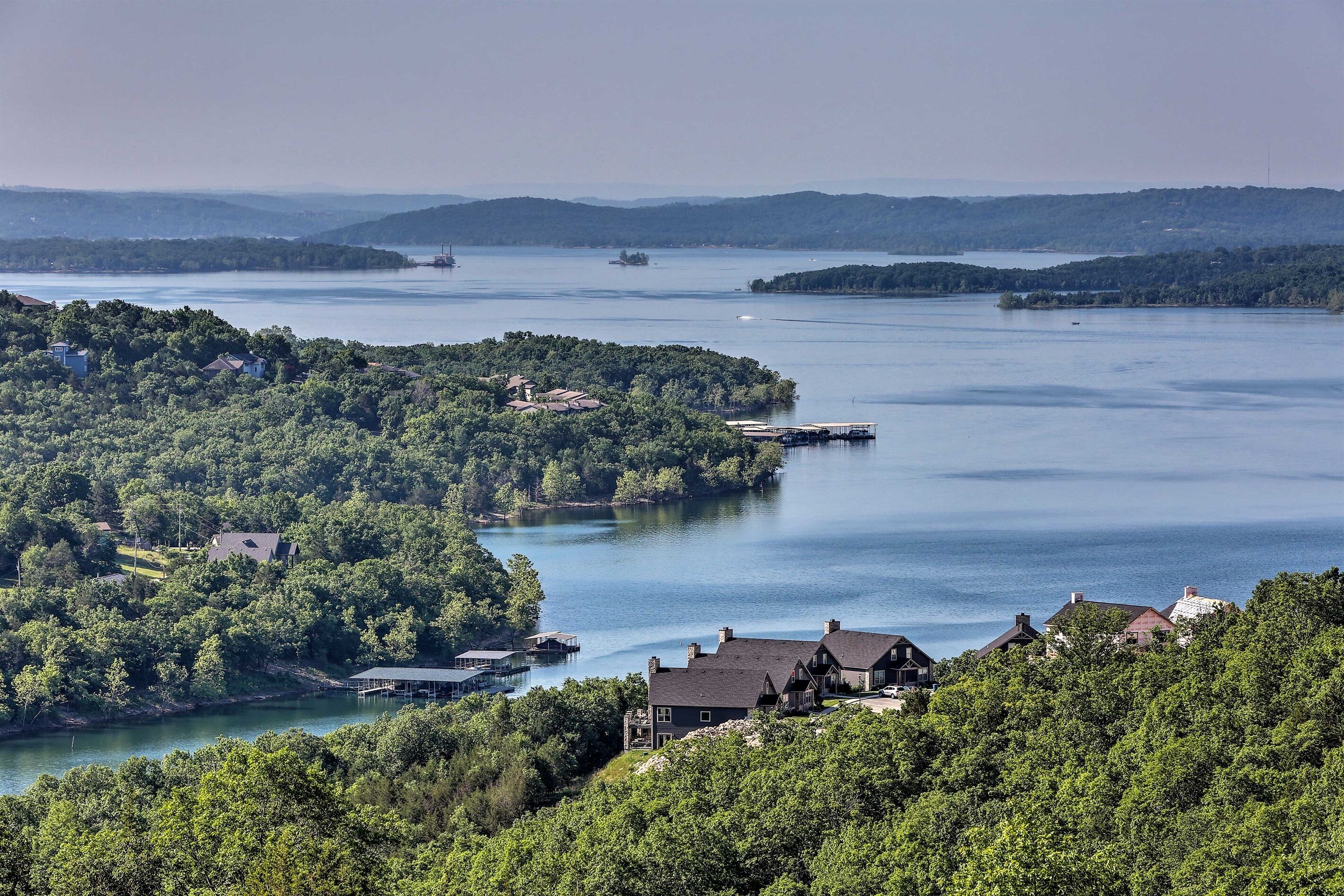 Ejendom ved søen med flere huse, bådebroer og et skovområde.
