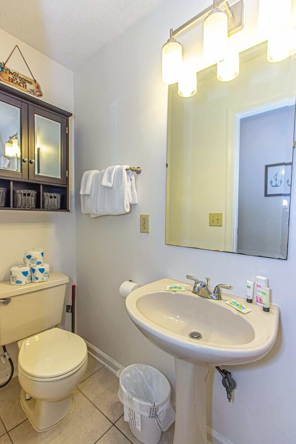 A bathroom with a toilet, sink, and mirror. There are towels hanging on the wall, and a basket of toiletries on the counter.