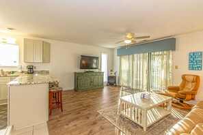 Un salon comprenant un canapé, une table basse, un téléviseur et un coin cuisine avec des placards et une cuisinière.