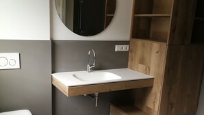 A modern bathroom with a white sink, a round mirror, and a wooden vanity. - Ferienwohnung Pusteblume Beilngries (Beilngries)