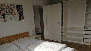 A bedroom with a wooden bed, white bedding, a nightstand, a lamp, and a wardrobe with open doors. - Ferienwohnung Pusteblume Beilngries (Beilngries)