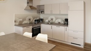 A modern kitchen with white cabinets, a stainless steel range hood, and a dining table with chairs. - Ferienwohnung Pusteblume Beilngries (Beilngries)