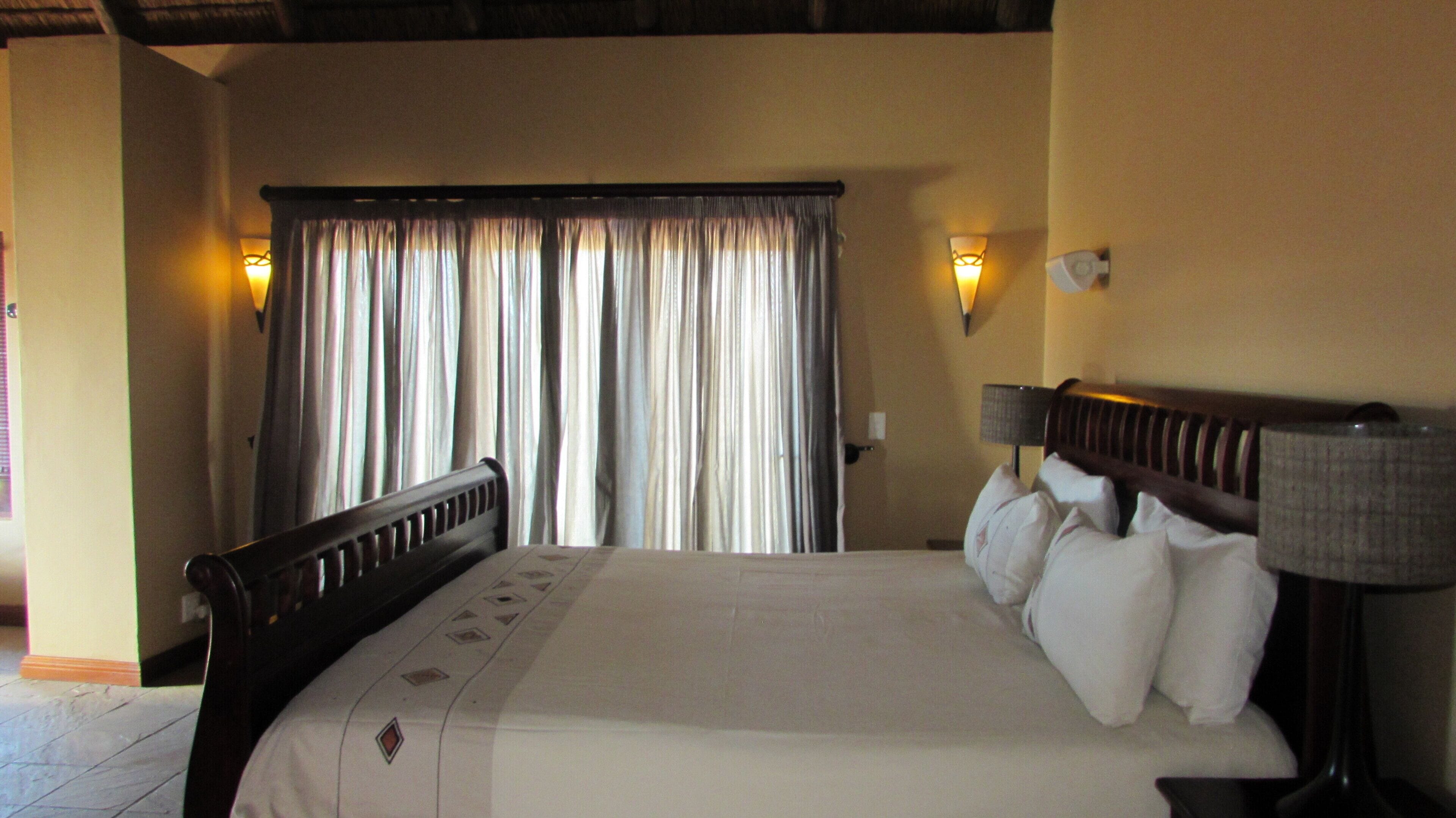 A hotel room with a bed, curtains, wall-mounted lamps, and a wooden headboard.