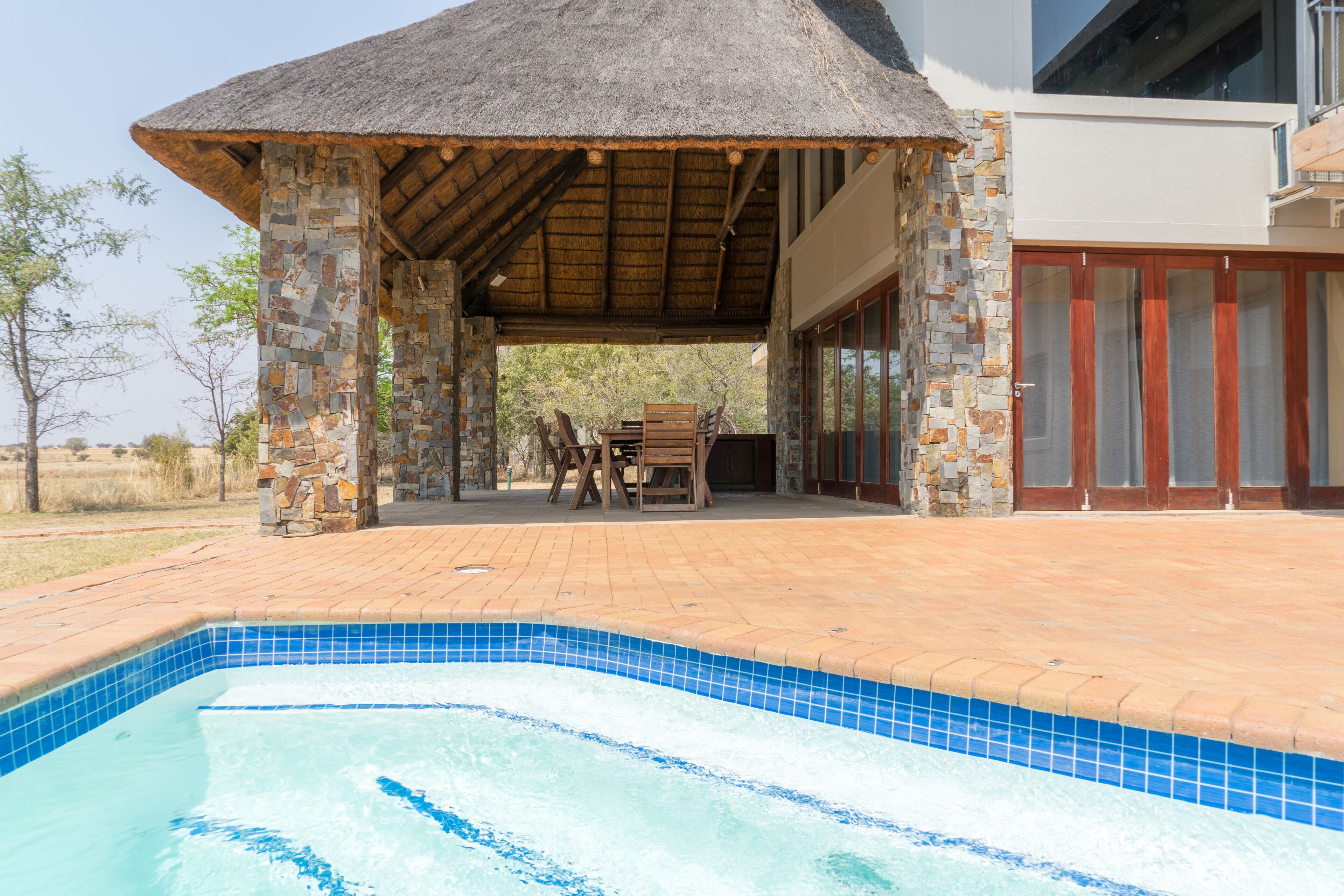 Un área de piscina con una estructura de piedra, muebles de madera y una puerta de vidrio.
