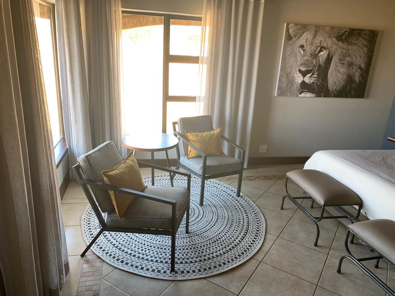 Habitación de hotel con cama, dos sillas, una mesa redonda y un ventanal con cortinas.