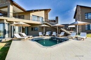 Uma casa moderna com piscina, espreguiçadeiras e guarda-sóis.