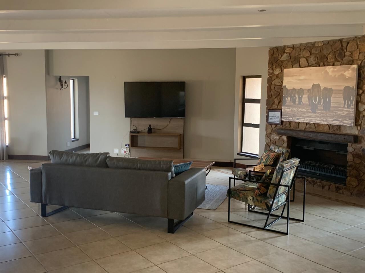 A spacious living room with a grey sofa, a fireplace, and a flat-screen TV mounted on the wall.