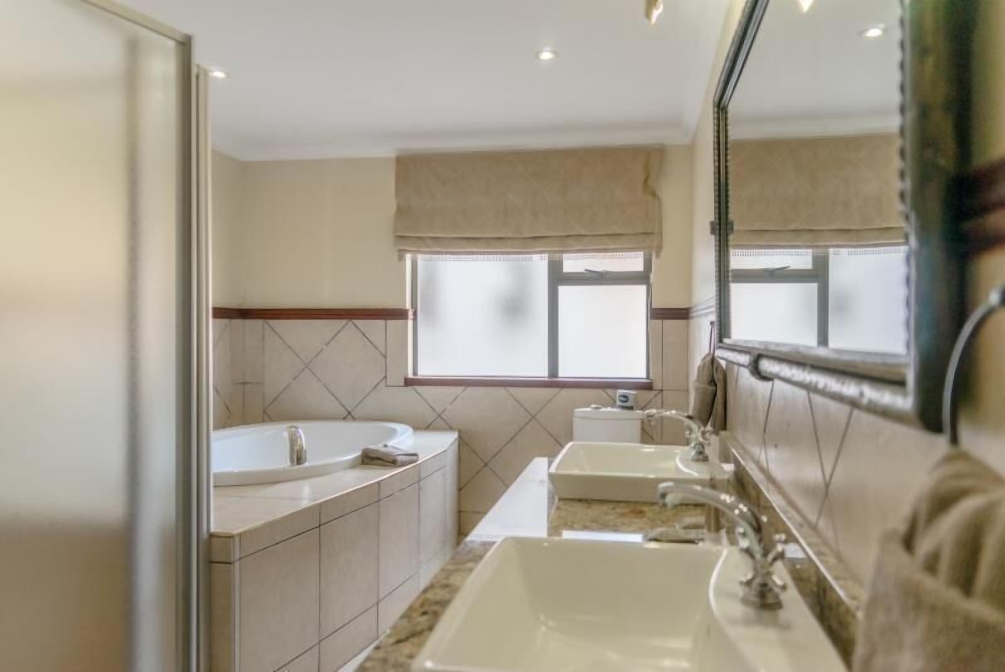 Un baño moderno con un espejo grande, una bañera, dos lavamanos y un ventanal con vistas.