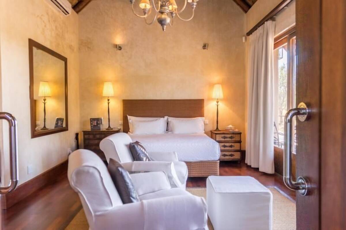 Een slaapkamer met een groot bed, twee nachtkastjes met lampen, een stoel, een klein tafeltje en een spiegel aan de muur.
