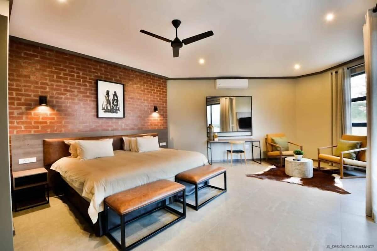 Een moderne slaapkamer met een accentmuur van baksteen, een groot bed, een bureau en een zithoek met stoelen en een bank.