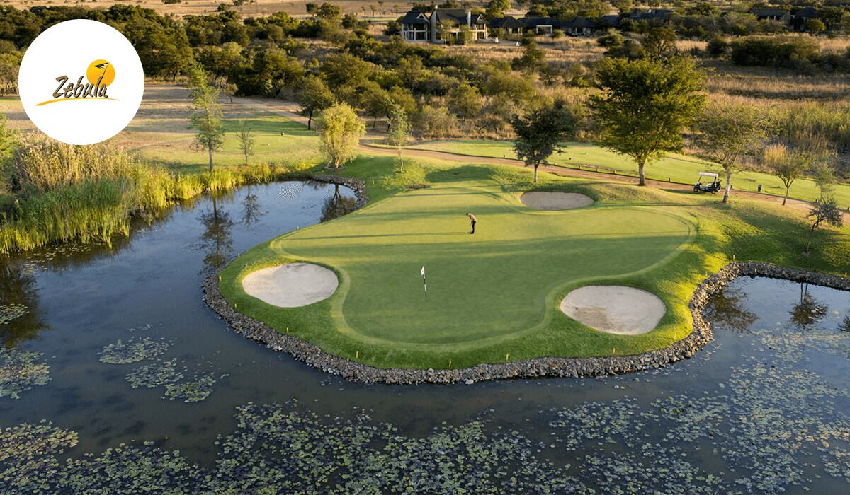 Un campo de golf con un estanque, búnkeres de arena y un club de campo al fondo.
