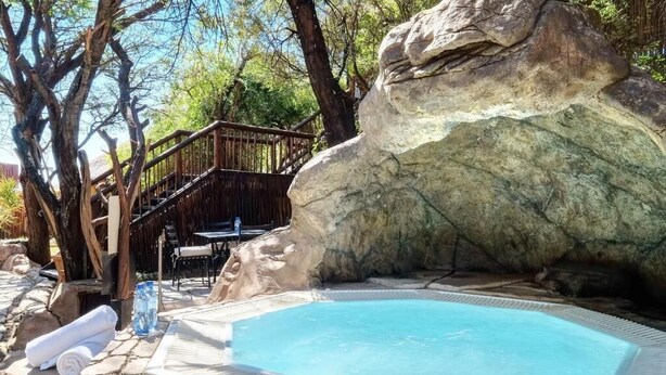 Un jacuzzi rodeado por un muro de piedra, con una terraza de madera y una escalera que lleva a otra zona con terraza de madera.