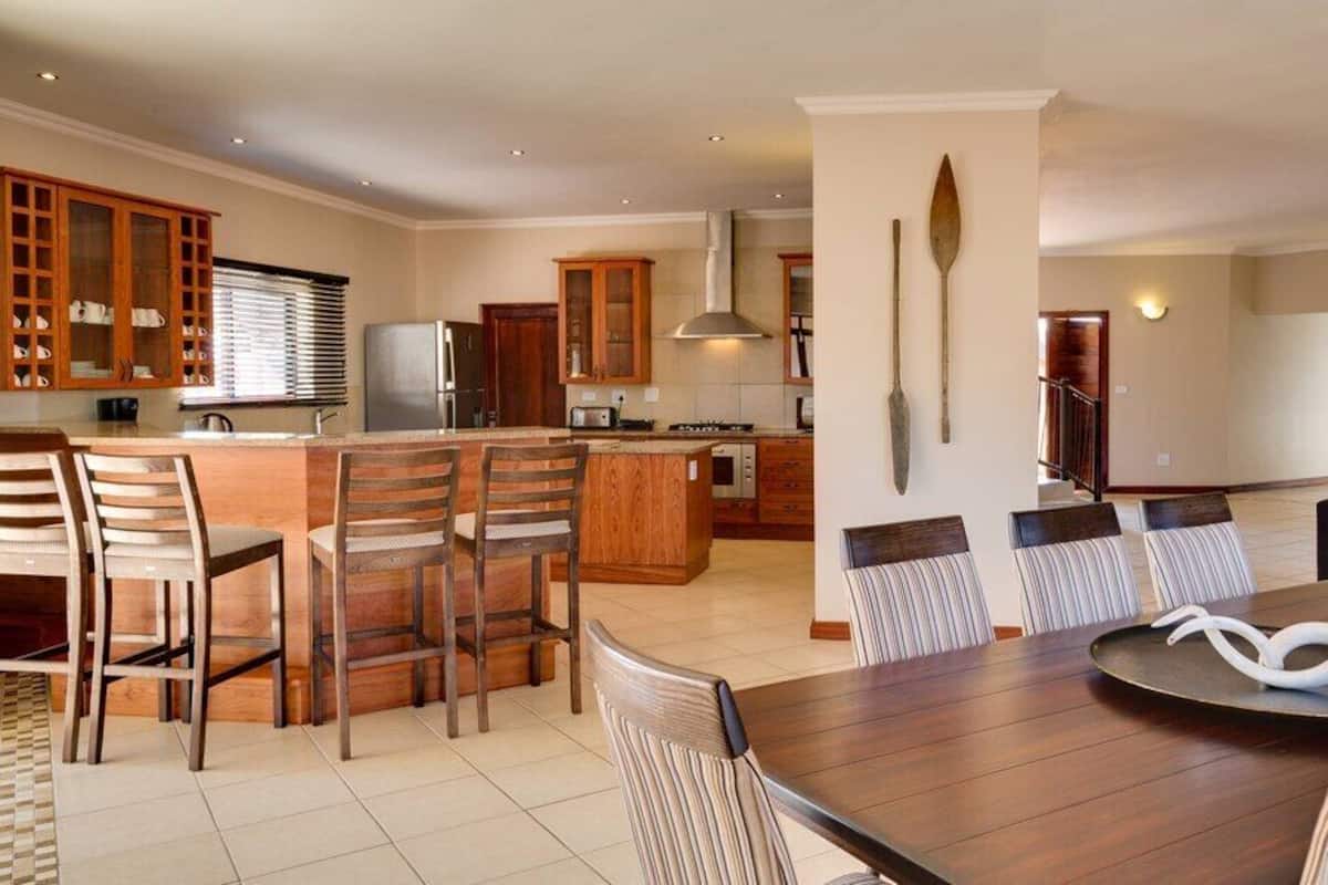 Een moderne keuken met houten kastjes, een centraal eiland met barkrukken, en een eethoek met gestreepte stoelen.