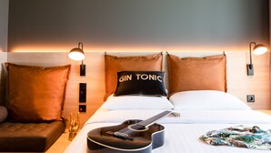 A hotel room with a bed, a guitar, a pillow with "GIN TONIC" text, and two wall-mounted lights. - Moxy Utrecht (Utrecht)