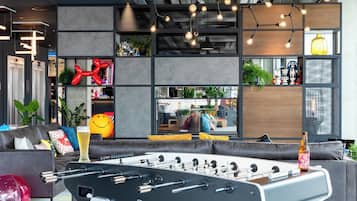 A modern indoor space with a foosball table, seating area, and decorative elements like a smiley face balloon and a bottle.