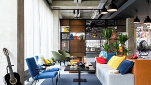 A modern lounge area with a sofa, chairs, a coffee table, and a guitar. - Moxy Utrecht (Utrecht)