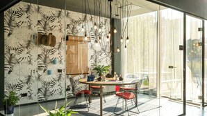 A modern dining area with a glass partition, a round table with red chairs, and a ceiling light fixture. - Moxy Utrecht (Utrecht)