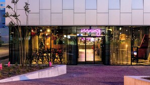 A modern building with a glass facade, a neon sign, and bicycles parked outside. - Moxy Utrecht (Utrecht)