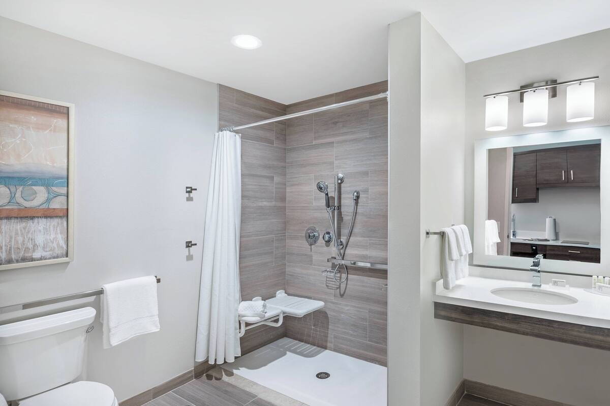 Ein modernes Badezimmer mit Dusche, Toilette und Waschbecken, ausgestattet mit einer Holzvertäfelung und einem großen Spiegel.