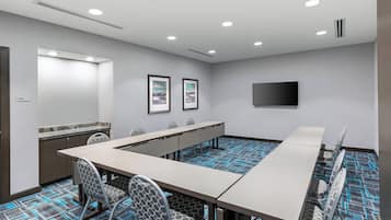A conference room with a long table, chairs, a flat-screen TV, framed pictures on the wall, and patterned carpet.