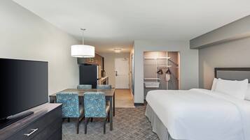 A hotel room with a bed, a TV, a desk with chairs, a kitchenette, and a bathroom.