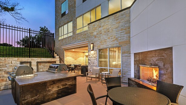 An outdoor patio with a stone wall, a grill, and a fire feature.