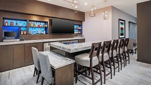 A modern kitchen with a bar area, marble countertops, and a large flat-screen TV.