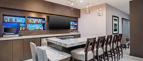 A modern kitchen with a bar area, marble countertops, and a large flat-screen TV.