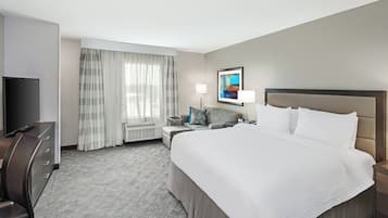 A hotel room with a large bed, a desk with a chair, a TV, a lamp, and a window with curtains.