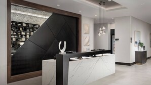 A modern reception area with a marble counter, a large black geometric wall, and a view of a cityscape through a window.