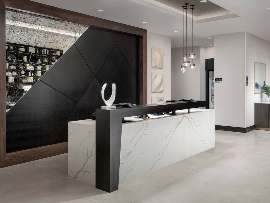 A modern reception area with a marble counter, a large black geometric wall, and a view of a cityscape through a window.