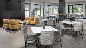 A modern indoor space with a fireplace, sofas, and dining tables.
