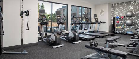 A gym with treadmills, weight machines, and a wall with exercise equipment.