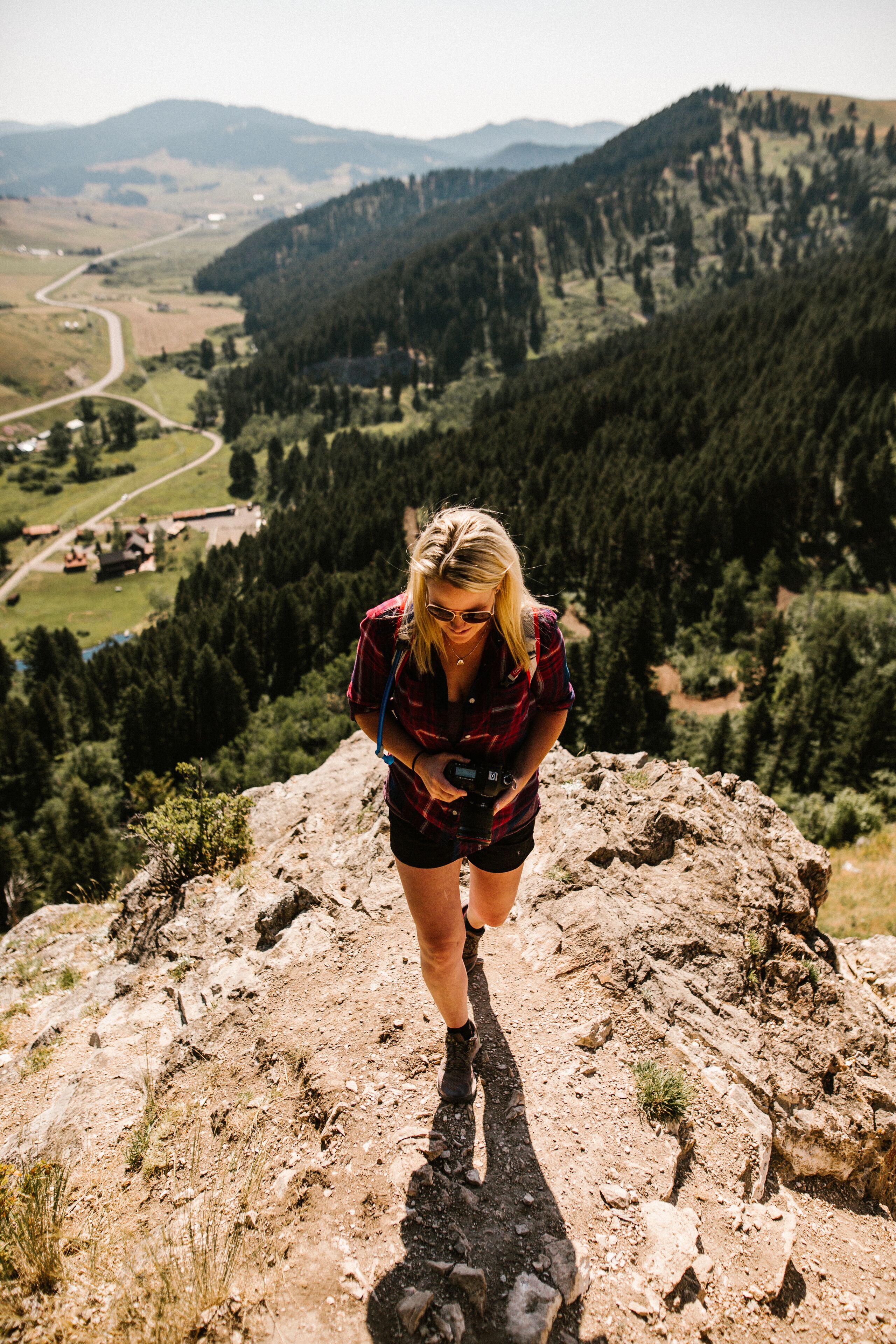 A person standing on a rocky outcrop overlooking a valley with a road and buildings in the distance.