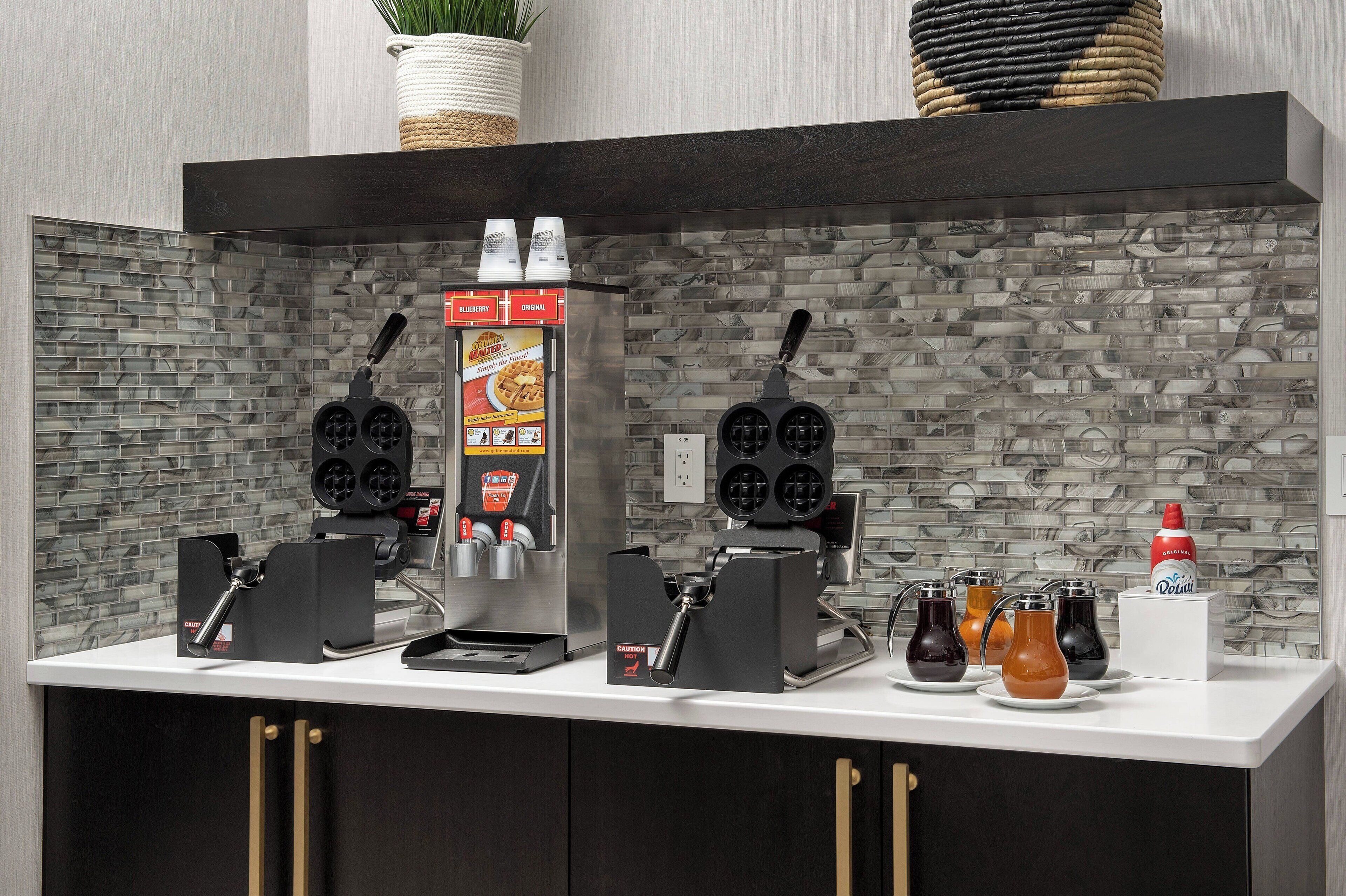 A coffee station with two espresso machines, a waffle maker, and a waffle display.