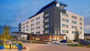 A modern hotel with multiple floors, a covered entrance, and a parking area with cars. - Aloft by Marriott Trophy Club Westlake (Roanoke)