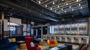 A modern lounge area with seating, a bar, and a large window displaying a colorful interior. - Aloft by Marriott Trophy Club Westlake (Roanoke)
