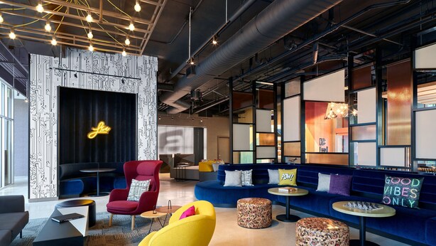 A modern lounge area with a sofa, red and yellow chairs, and a neon sign. - Aloft by Marriott Trophy Club Westlake (Roanoke)
