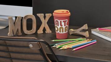 Letras de madera que deletrean “MOX” sobre un escritorio, una taza roja de café con el logotipo “ALT” y lápices de colores.