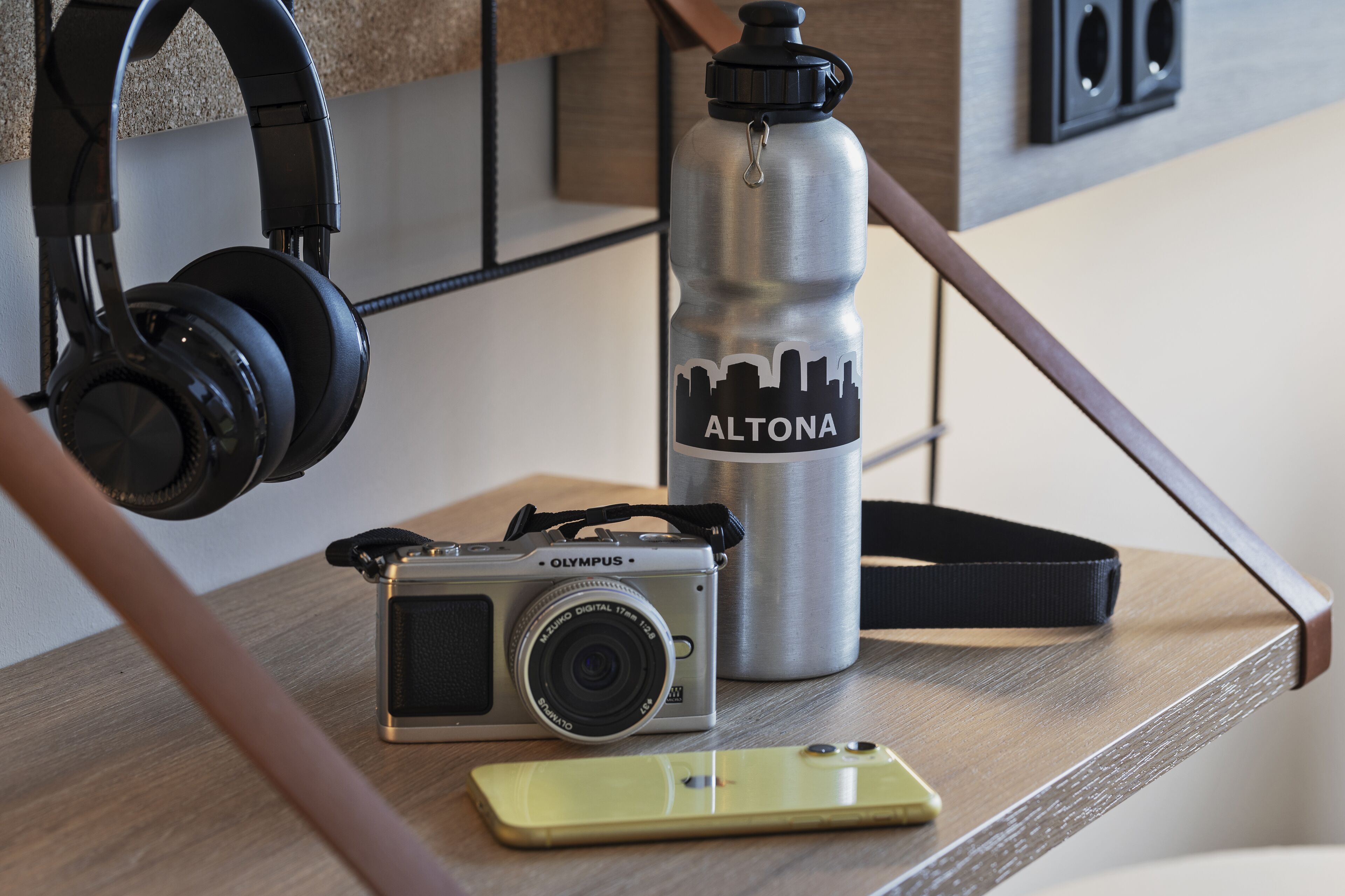 Eine Kamera, Kopfhörer, eine Wasserflasche und ein Smartphone auf einer Holztisch.