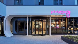 A modern building with a glass entrance and a neon sign that reads "mozy". - Moxy Hamburg Altona (Hamburg)