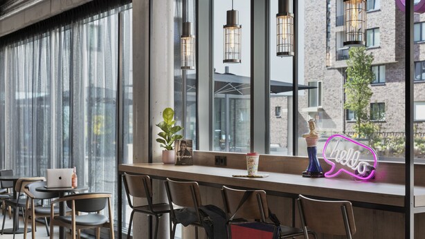 A modern bar area with a laptop, a neon 'hello' sign, and a potted plant. - Moxy Hamburg Altona (Hamburg)