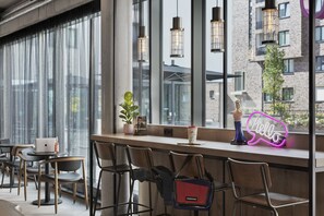 A modern bar area with a laptop, a neon 'hello' sign, and a potted plant. - Moxy Hamburg Altona (Hamburg)