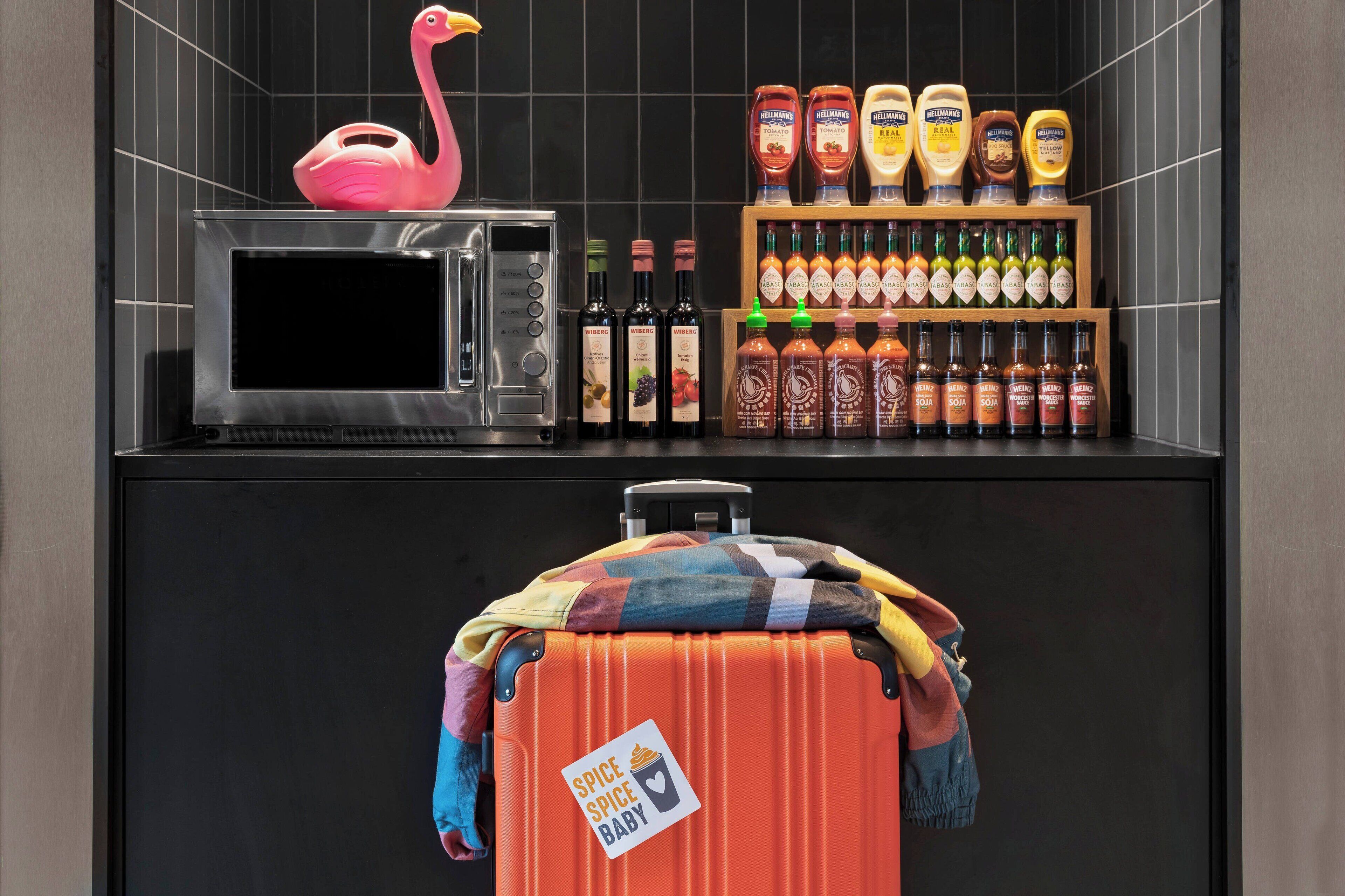 A kitchen with a microwave, a shelf of condiments, and a suitcase with a 'Spice Baby' label.