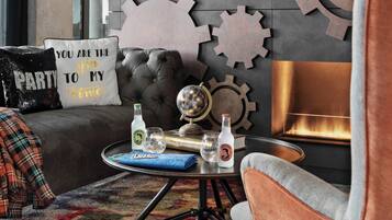 Una sala de estar acogedora con un sofá de cuero, una mesa de centro redonda con bebidas y un libro, engranajes decorativos en la pared y una chimenea.